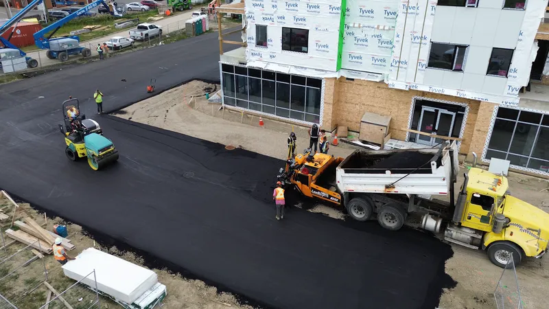 Roller, paver and dump truck placing hot mix asphalt at a building entrance