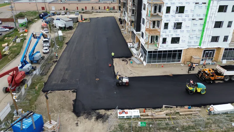 Aerial of a new asphalt parking lot being rolled beside a multi-family building