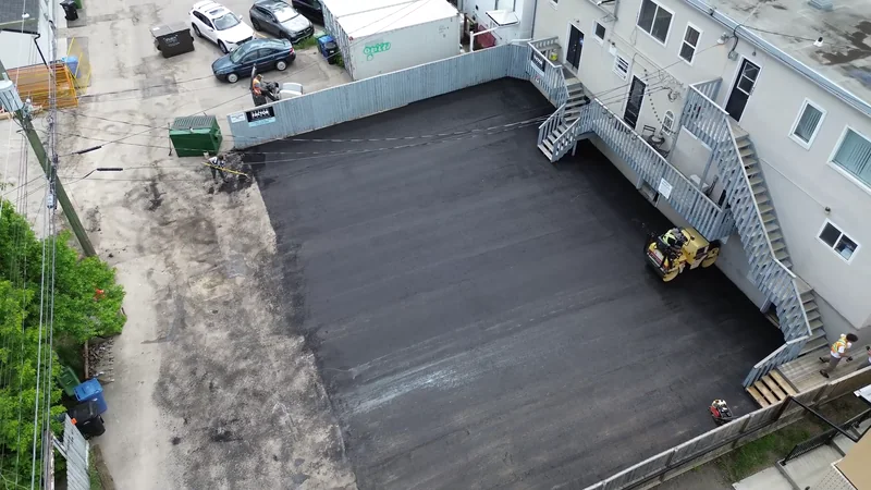 Aerial of a freshly repaved rear parking lot behind a Calgary commercial building, roller still on site