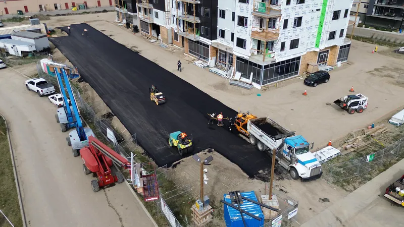 High aerial of a Calgary-area paving job: dump truck, paver and roller on the new asphalt
