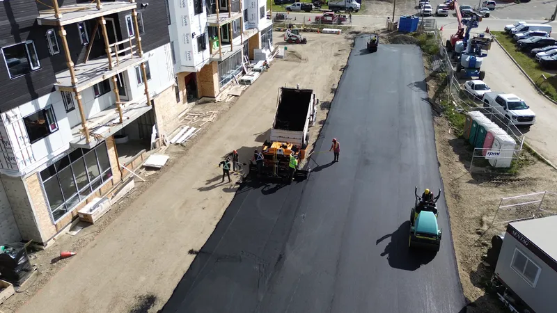 Aerial view down a new asphalt drive lane toward the paver, crew and roller