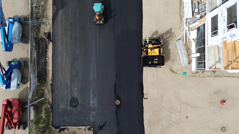 Straight-down aerial of a fresh hot mix asphalt strip with the paver and roller at work