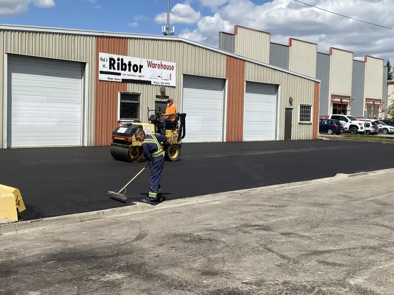 Commercial Paving crew rolling and raking new hot mix asphalt at a Calgary warehouse lot