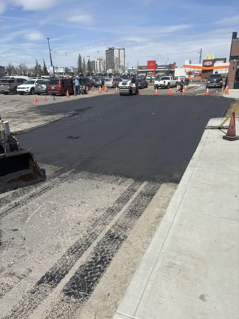Fresh hot mix asphalt patch being compacted at a Calgary commercial parking lot